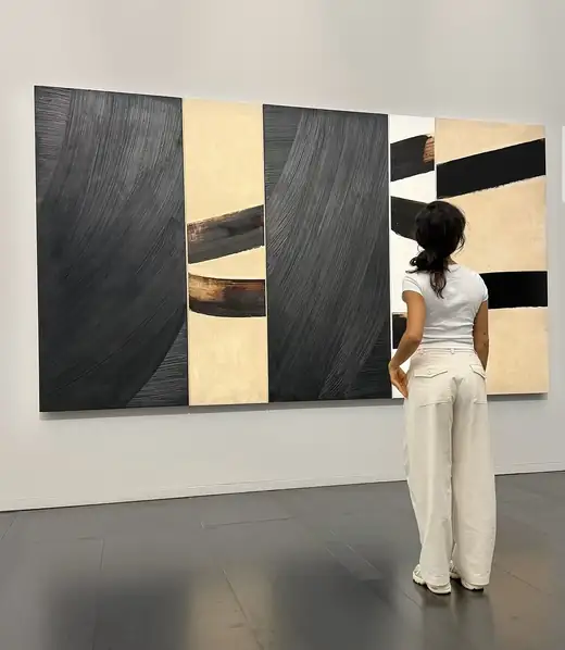 Une visiteuse devant une grande toile noire et beige de Pierre Soulages